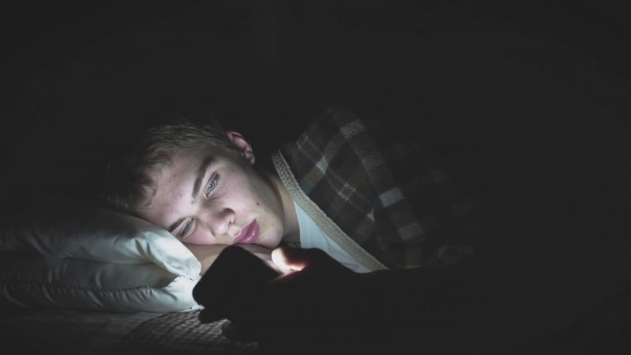 A teenager looking at a phone in bed at night