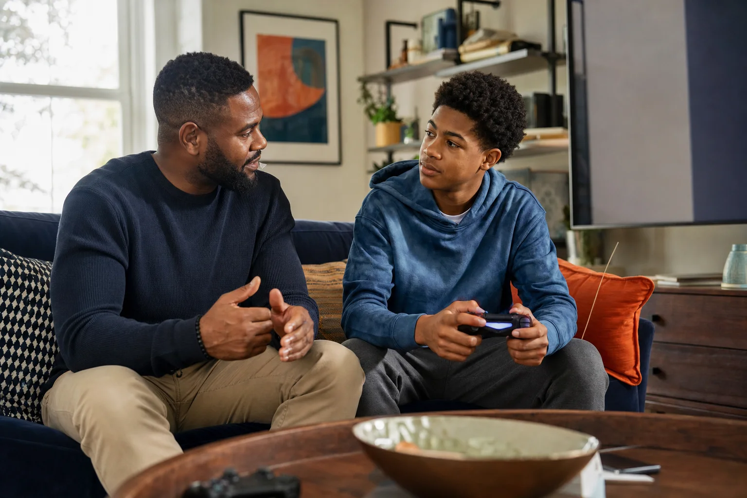 A father listening to his teenage son explain a video game while holding a controller