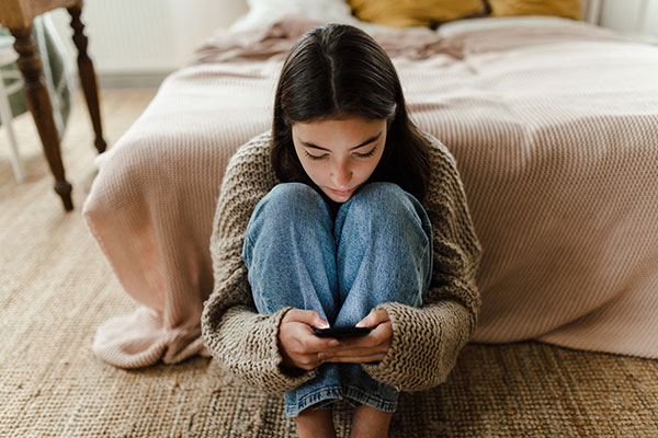 Teenager sitting on the floor looking at her phone near her bed