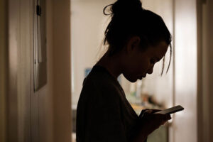 Cyberbullying, young woman looking at her phone while in the shadows